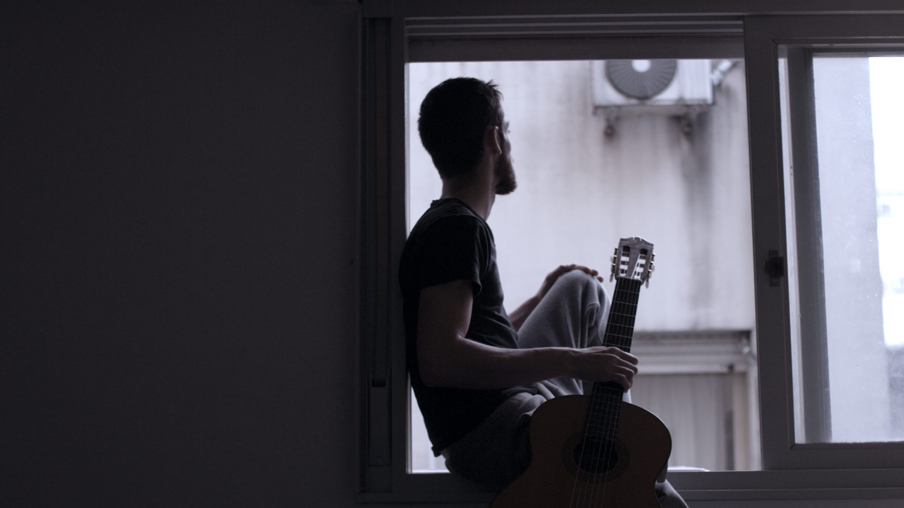 A musician with his guitar, backlit in front of a window
